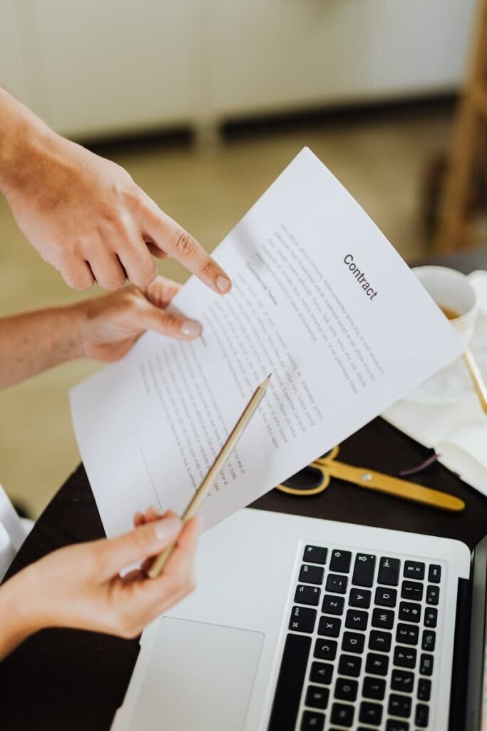 Hands pointing at contract on desk with laptop, indicating collaboration