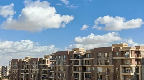 Spacious modern apartment buildings under a bright blue sky with fluffy clouds.